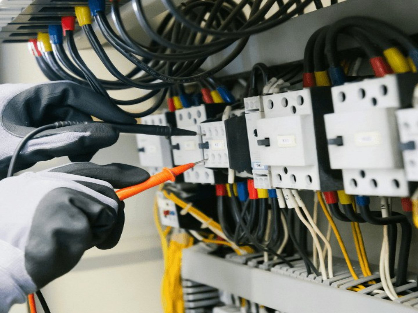 Ręce technika w rękawiczkach testują panel elektryczny multimetrem.