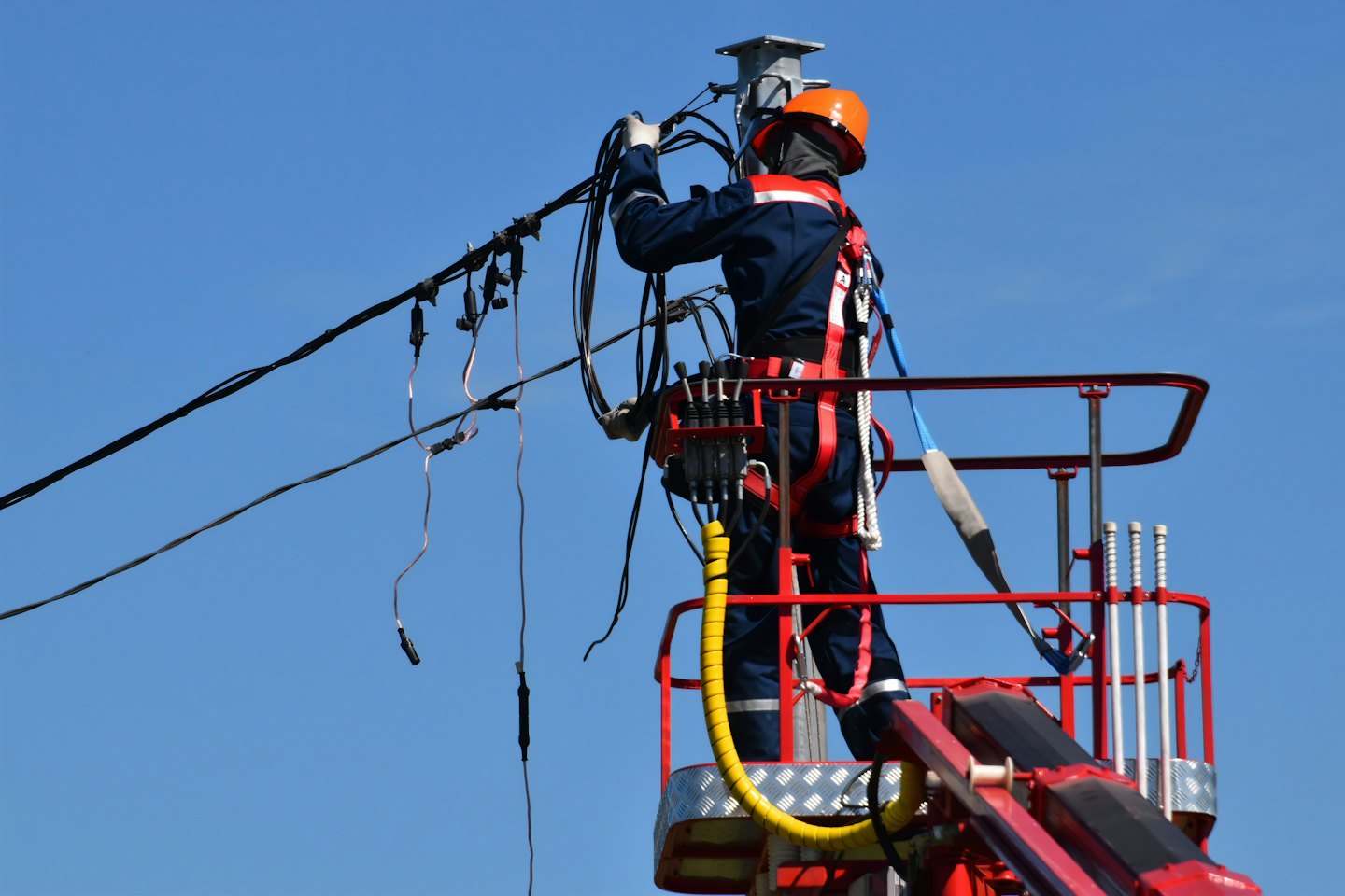 Elektryk w pomarańczowym kasku pracuje przy przewodach z podnośnika koszowego.